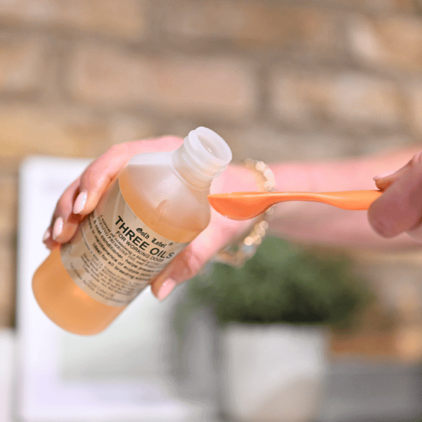 Person pouring Three Oils blend of Cod Liver, Evening Primrose, and Wheatgerm for dogs into a spoon, supporting skin and joint health.
