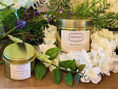 Pet friendly scented candles by Mollie Browns surrounded by white flowers and green leaves.