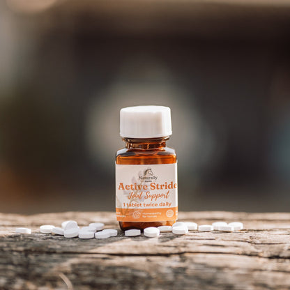 A small amber glass bottle with a white cap labeled 'Active Stride Joint Support' sits on a weathered wooden surface with scattered white tablets around it, against a softly blurred outdoor background.