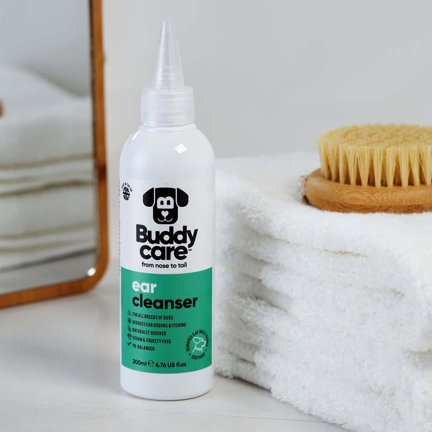 Buddy Ear Cleaner bottle with soothing aloe vera, PH-balanced formula for reducing wax buildup, next to a mirror and towels.