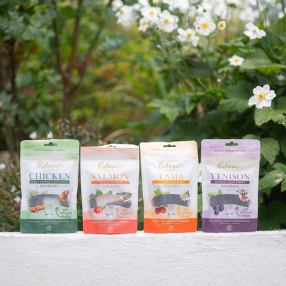 Eden Sausage Treats: chicken, salmon, lamb, and venison sausages in colorful packaging near flowers.