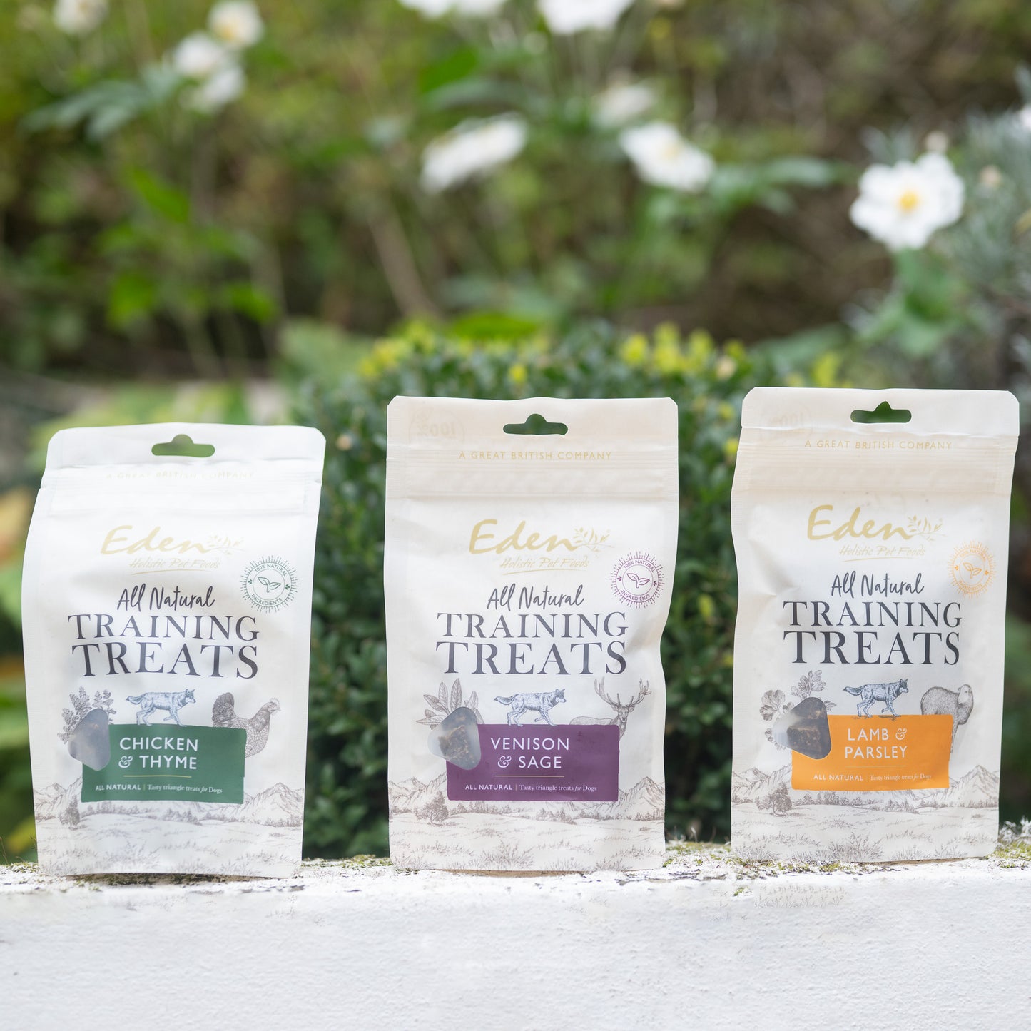 Eden Training Treats packaging for Chicken & Thyme, Venison & Sage, and Lamb & Parsley, displayed outdoors.