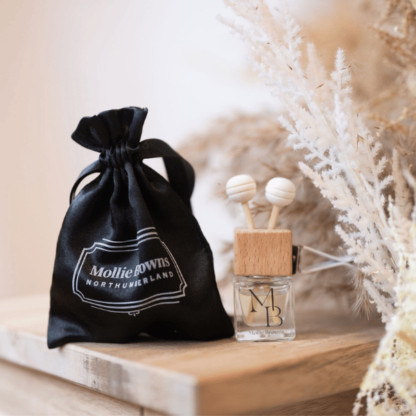 Car diffuser bottle on table with black satin presentation pouch next to it