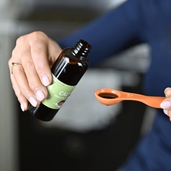 Person pouring Calm Dog Hemp Oil into measuring spoon for anxious dogs' stress relief and healthy coat.