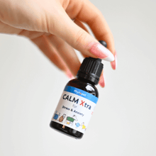 Hand holding bottle of Calm Xtra natural calmer for dogs with stress and anxiety.