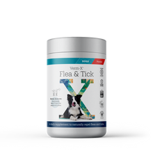 A white 70g tub of Verm-X Flea & Tick Powder for dogs, with a grey screw-top lid. The label features the product name, a black-and-white dog sitting in front of a large green and blue letter X, and text describing it as a daily supplement to naturally repel fleas and ticks. Badges on the right indicate certifications and that the product contains no artificial ingredients.