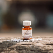 A small amber glass bottle labeled 'Equicalm Support' with a white cap, standing on a weathered wooden surface with scattered white tablets around it. The background is softly blurred.