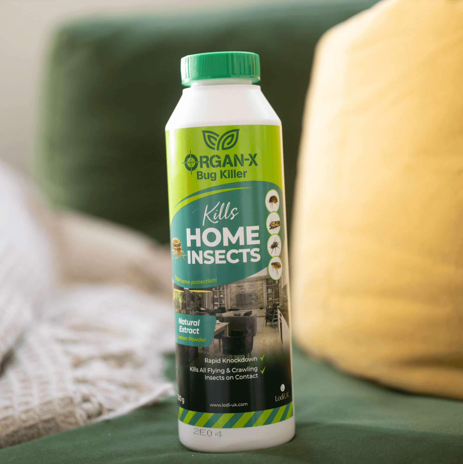 Organ-X Bug Killer bottle on a green couch, effective for home insect control with natural extract.