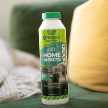 Organ-X Bug Killer bottle on a green couch, effective for home insect control with natural extract.